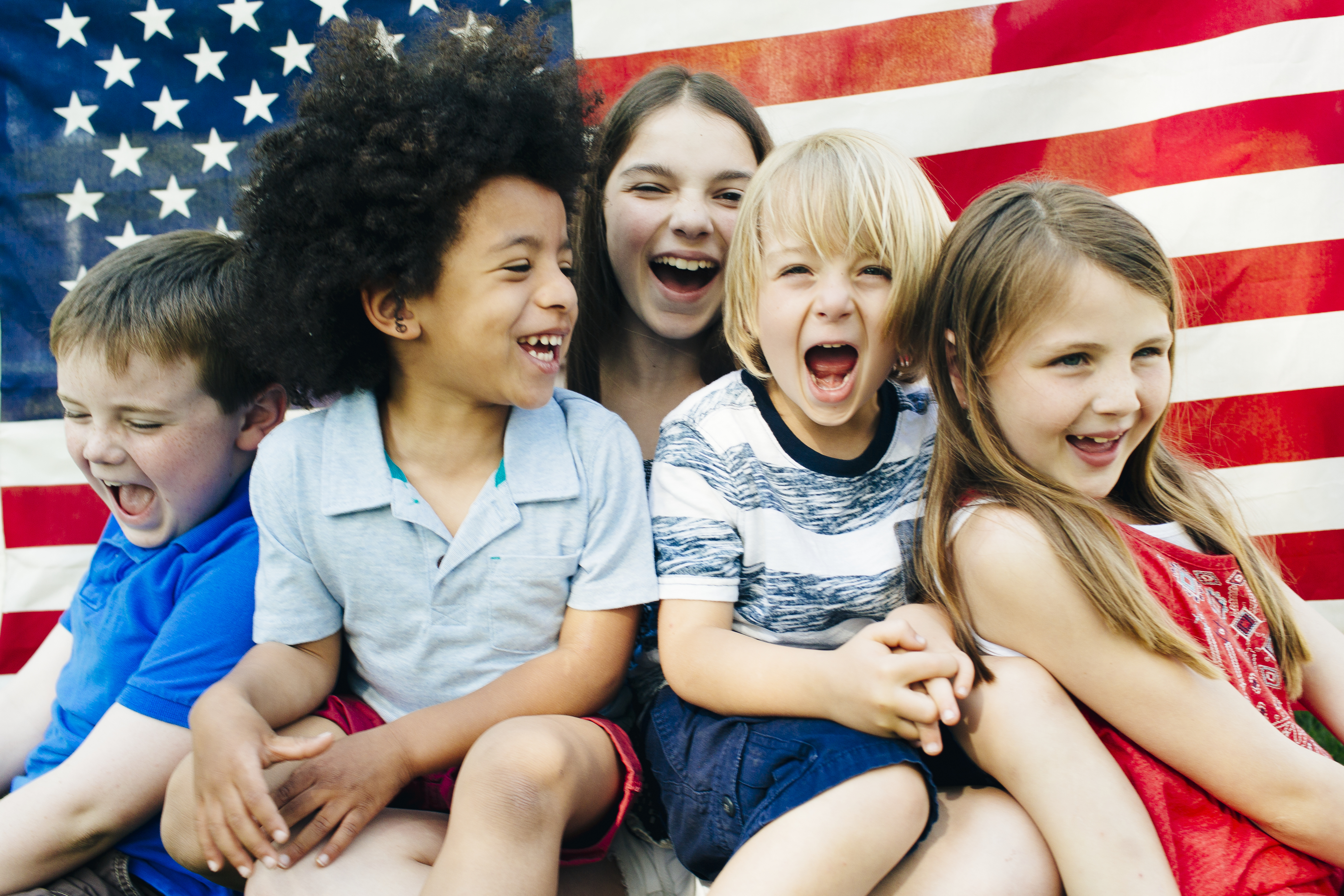 Group of laughing children (2-3, 4-5, 6-7) in front of American flag