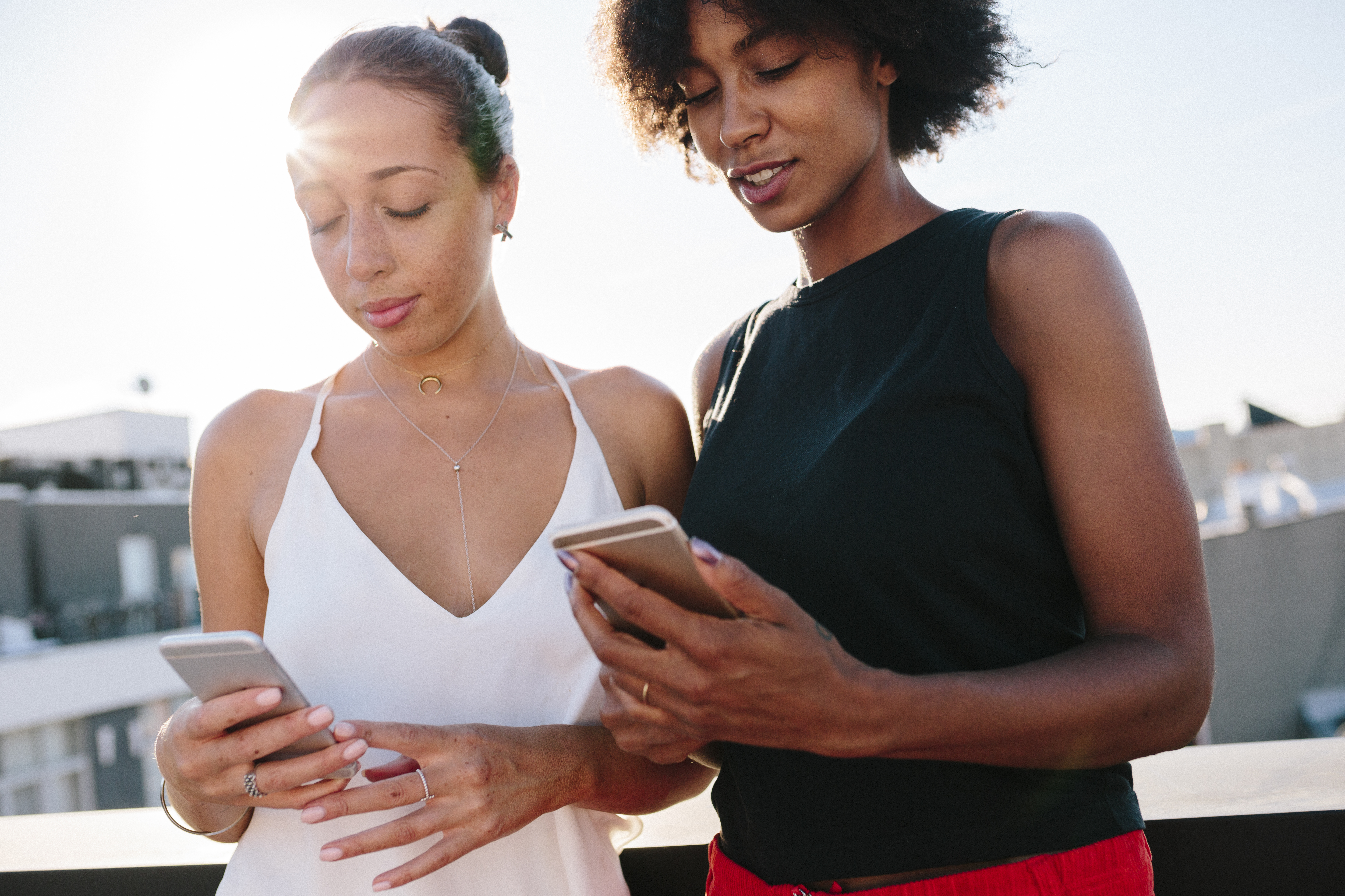 Female friends standing on rooftop using their smart phones