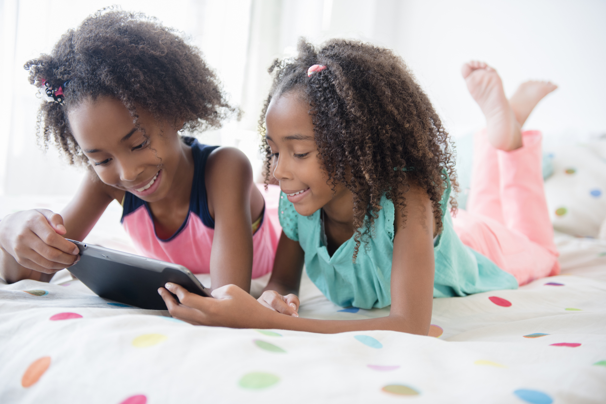 Mixed race sisters using digital tablet on bed